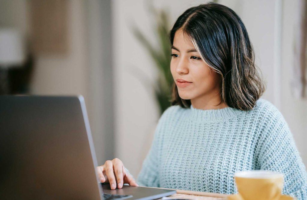 woman in light blue sweater using trackpad of laptop